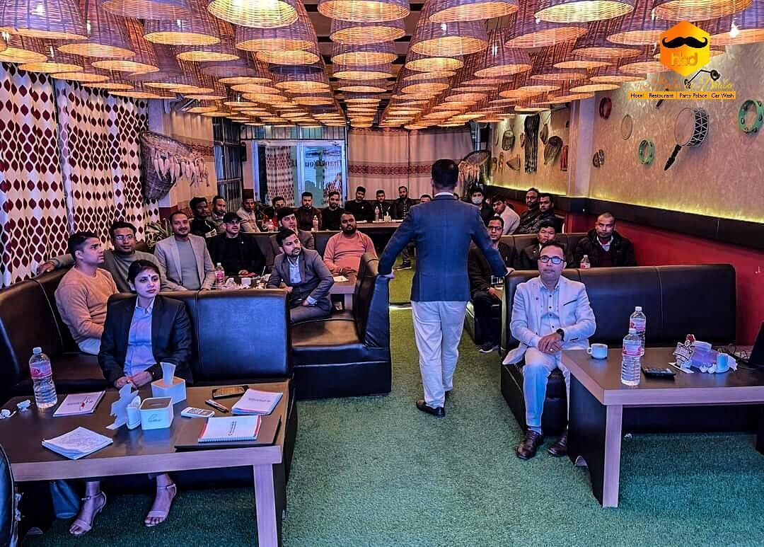 Una sala de conferencias con diseño moderno, que presenta un muro con textura, un techo alto con lámparas colgantes y una alfombra verde.