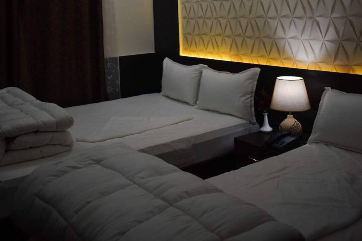 A hotel room with two beds, a nightstand with a lamp, and a geometric-patterned headboard.