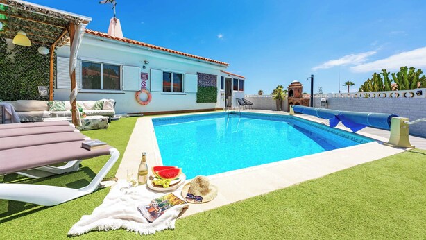 Un espace piscine avec une piscine à l’eau d’un bleu limpide, des chaises longues et une petite table sur laquelle se trouvent une pastèque et des boissons.