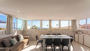Un salon moderne doté d’une grande table à manger, de sièges confortables et offrant une vue sur la plage.