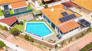 Vue aérienne d’un quartier résidentiel avec une piscine, des panneaux solaires et un patio couvert.
