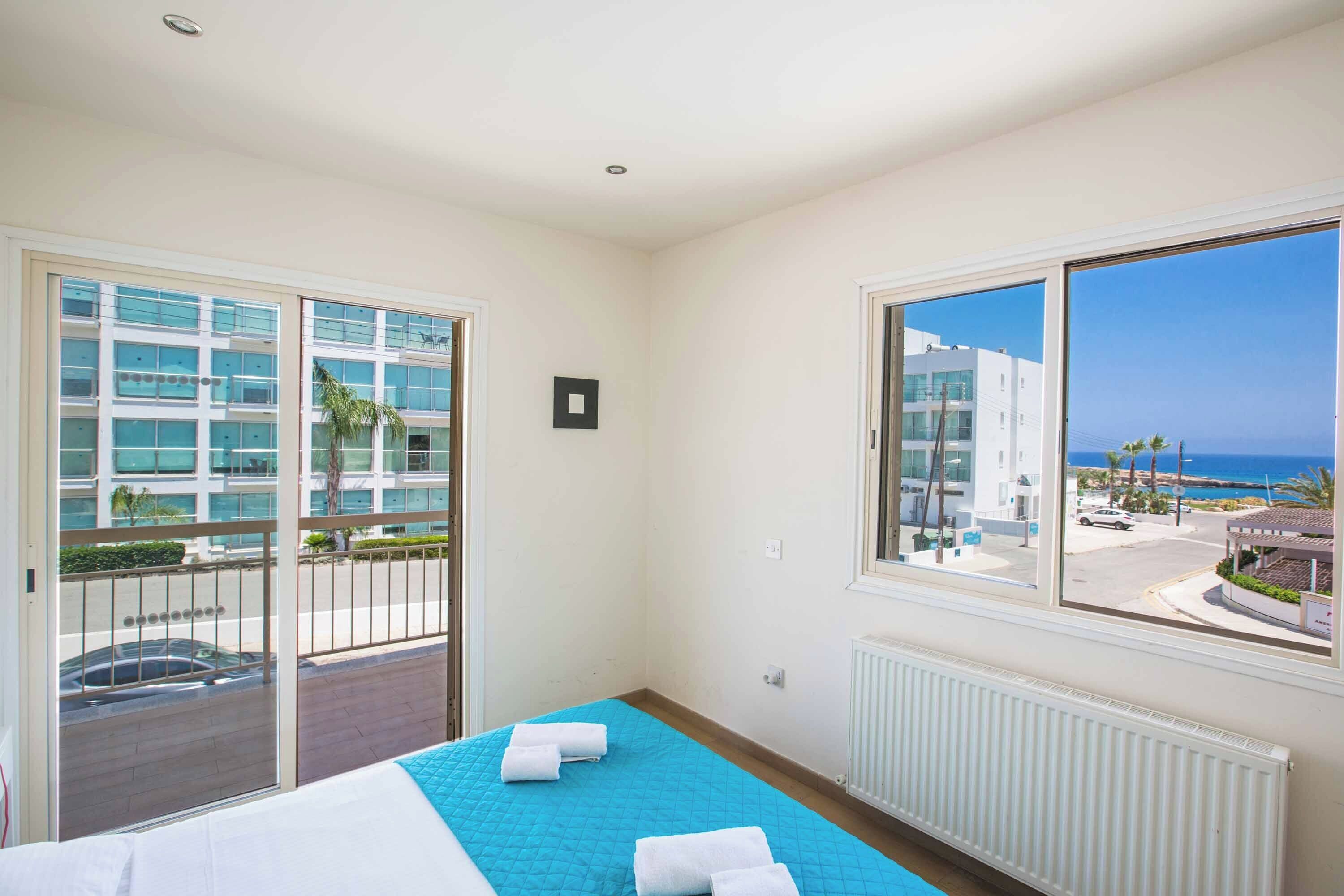Une chambre d’hôtel avec un lit, une grande fenêtre donnant sur la mer et un balcon avec un jacuzzi.