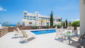 A rooftop pool area with lounge chairs and a table, overlooking a building and the sea. - Villa Delfini 16 - Four Bedroom Villa, Sleeps 8 (Protaras)