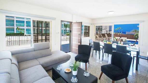 A modern living room with a sofa, chairs, and a coffee table. There is a balcony with a view of the ocean. - Villa Delfini 16 - Four Bedroom Villa, Sleeps 8 (Protaras)