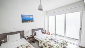 A hotel room with two beds, a large window, and a painting of a coastal scene. - Protaras Greco Villa CCV2 (Πρωταράς)