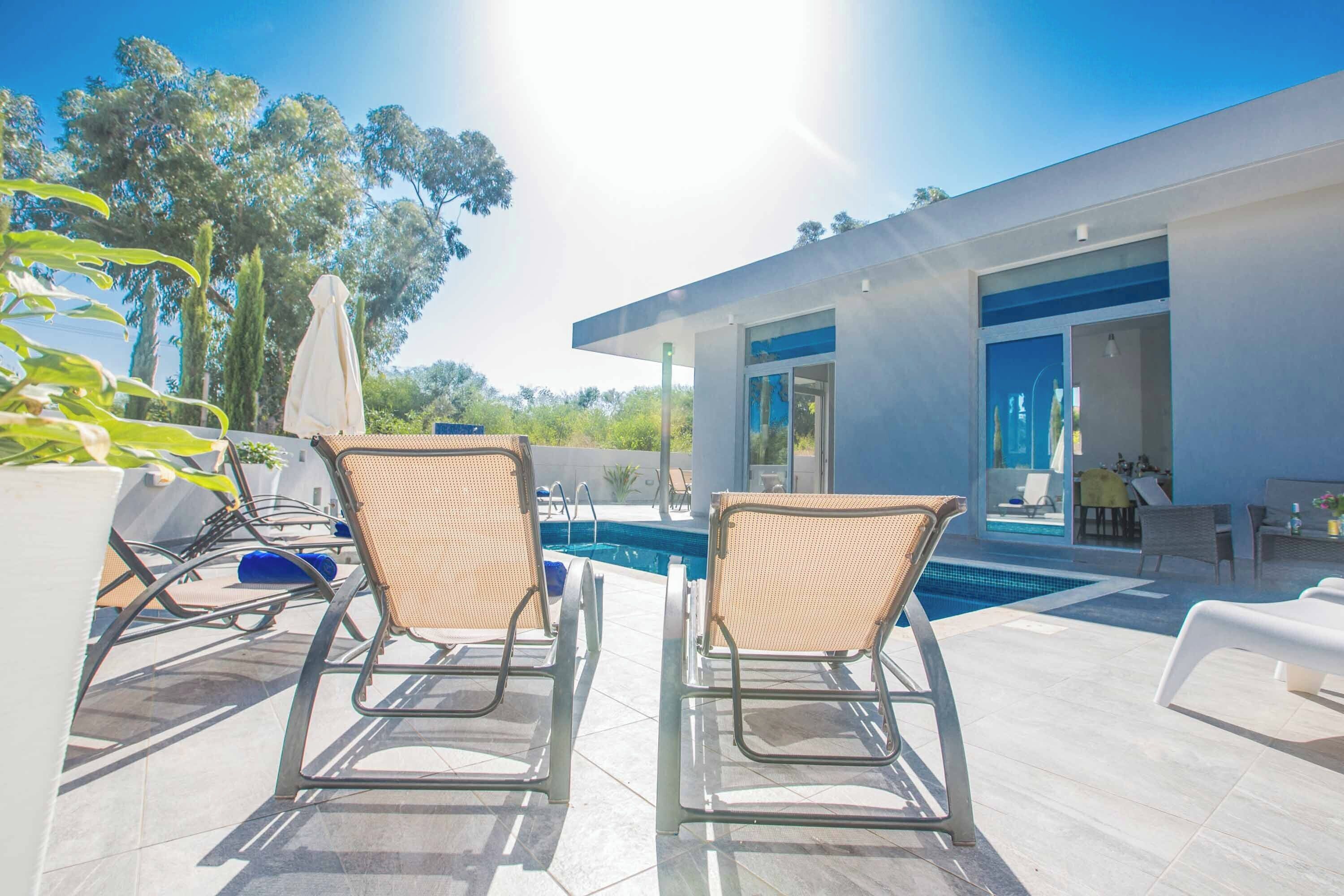 A modern outdoor pool area with two lounge chairs, a pool, and a contemporary building with large windows.
