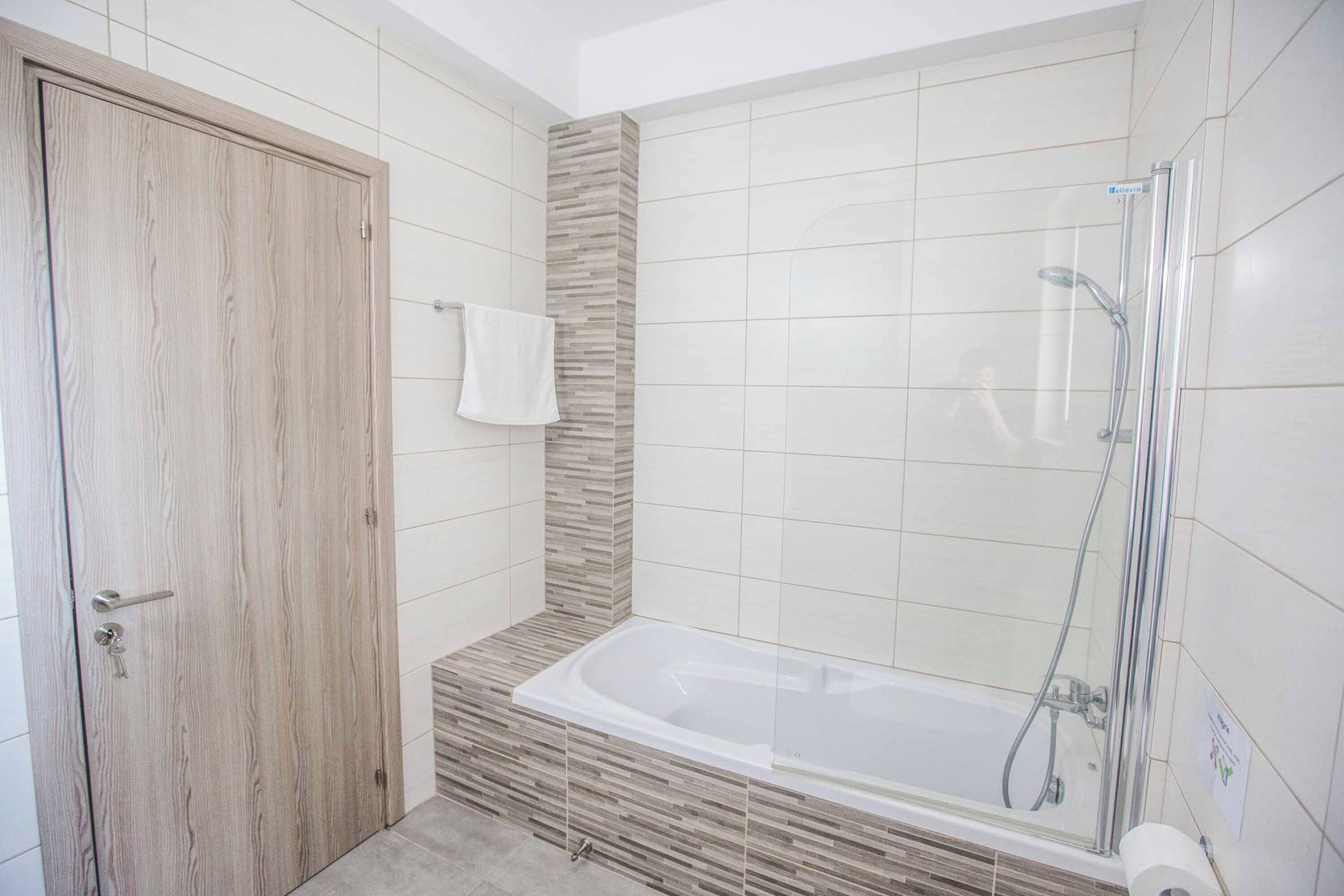 Un baño moderno con puerta de madera, ducha con cerramiento de vidrio y bañera empotrada.
