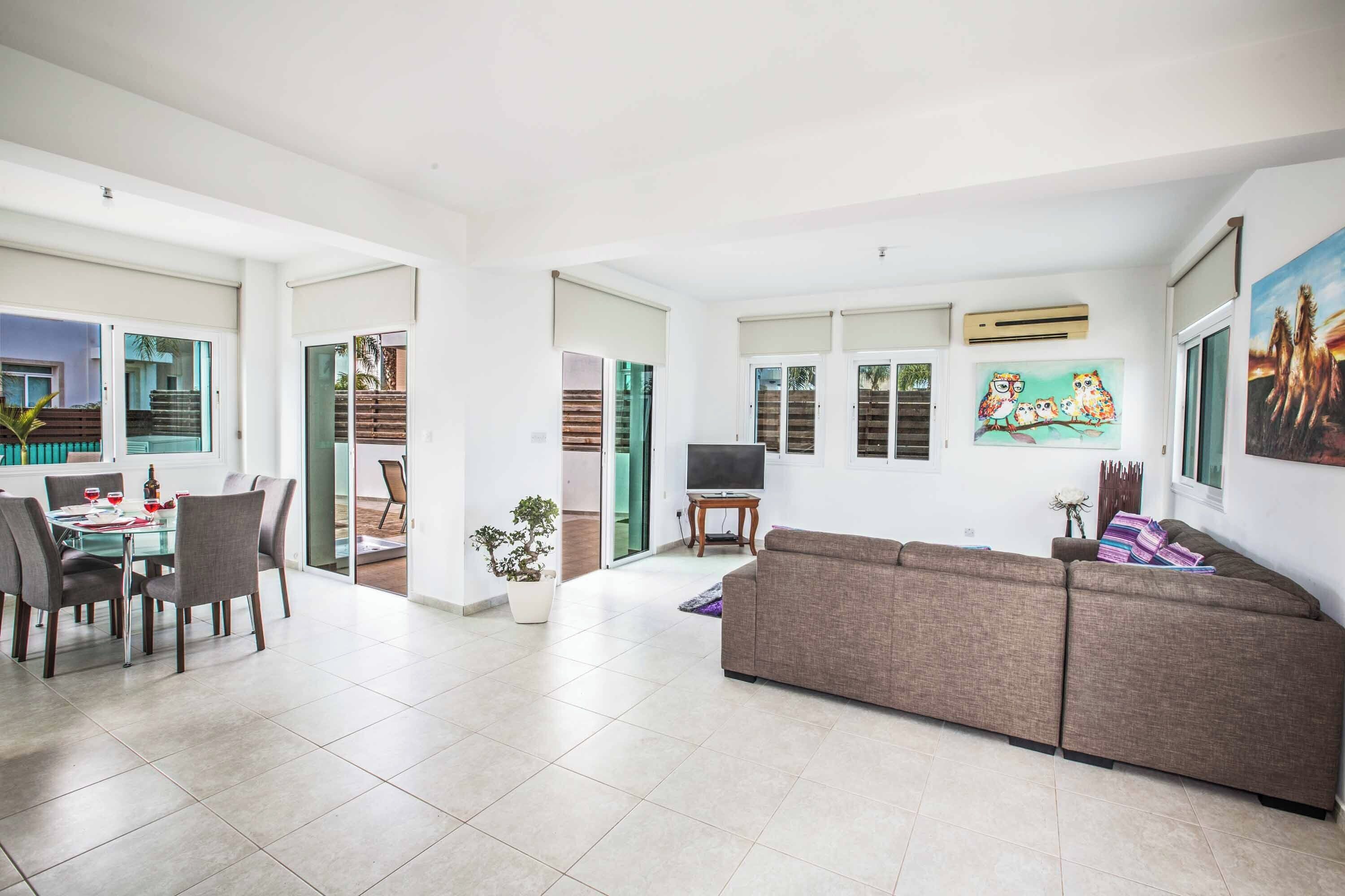A spacious living area with a dining table, chairs, a sofa, and a TV.