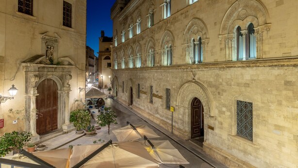 A courtyard with stone buildings, arched windows, and potted plants. - Royal Suite (Trapani)