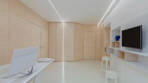 Une pièce moderne et bien éclairée, dotée d’un téléviseur à écran plat, d’un bureau avec un ordinateur et d’un coin salon avec des tabourets.