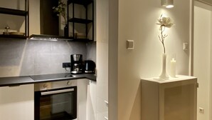 A modern kitchen with white cabinetry, a built-in oven, a coffee maker, and a small shelf with decorative items.