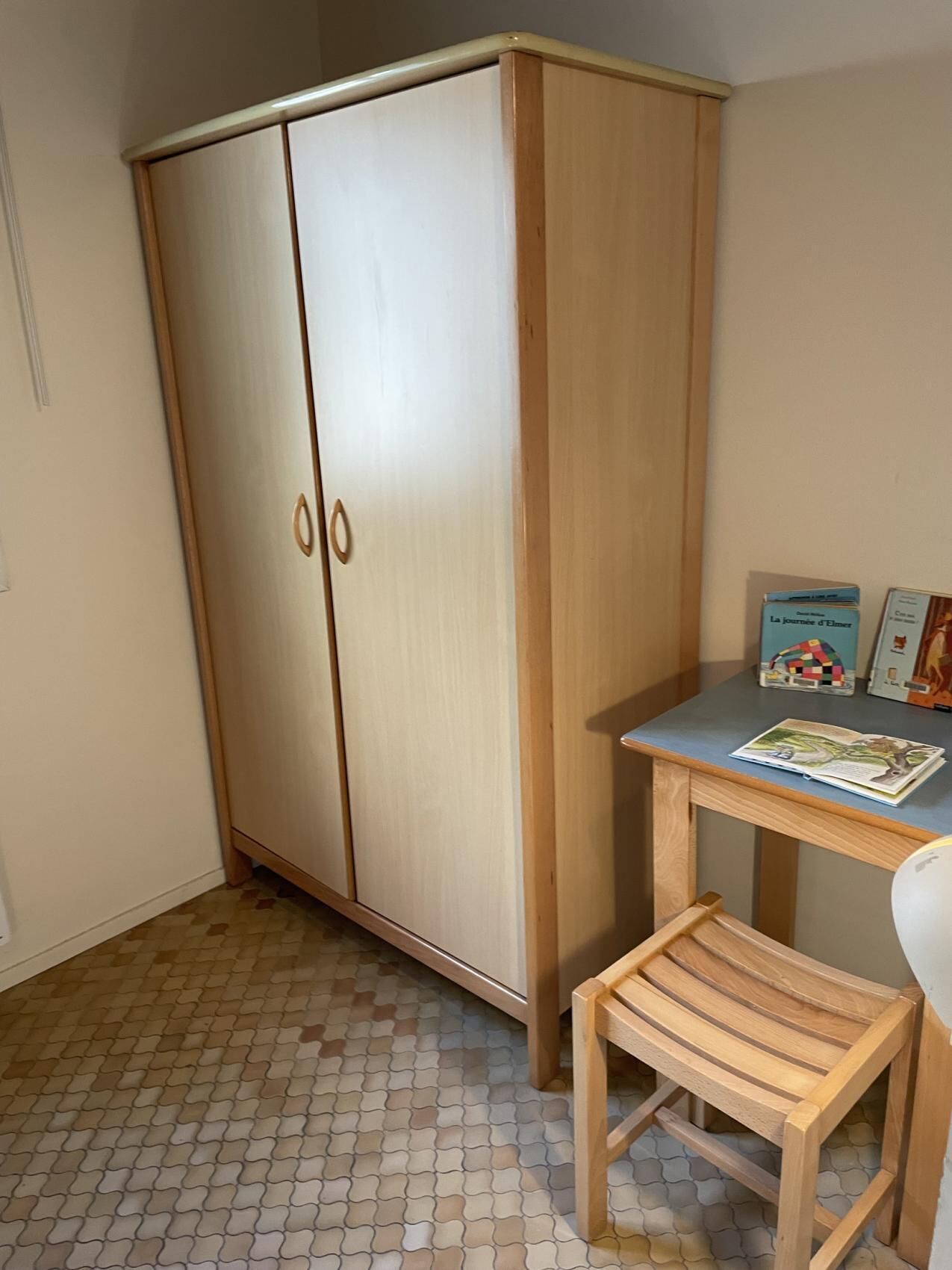 Une pièce comprenant une armoire en bois, une petite table en bois sur laquelle se trouve un livre, et un tabouret en bois.