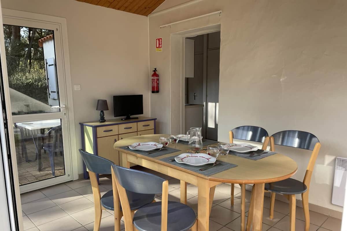 Ein Essbereich mit einem für sechs Personen gedeckten Tisch, umgeben von sechs Stühlen. Links befindet sich ein Fernseher auf einer kleinen Kommode.