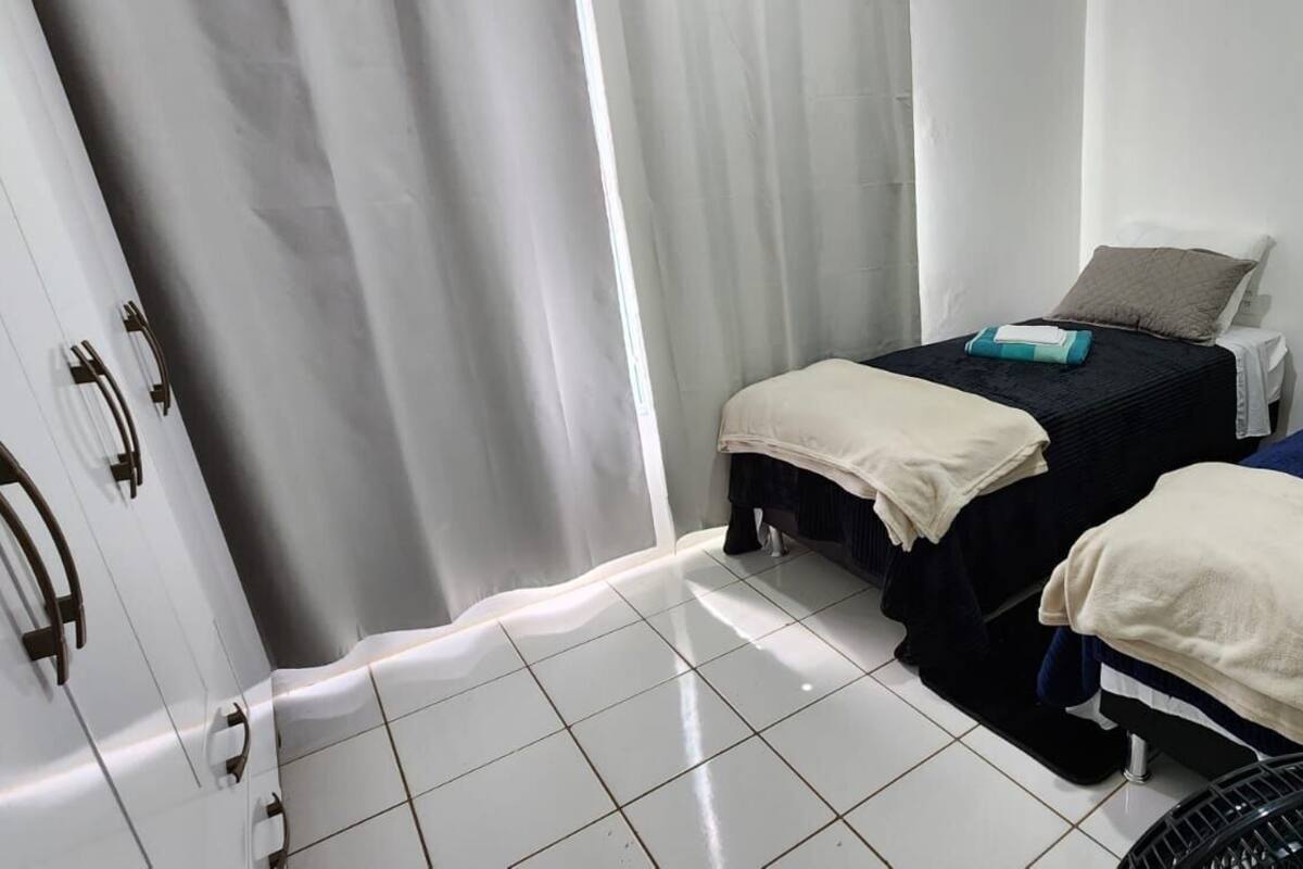 A hotel room with two beds, each with a pillow and a blanket. There is a door with a handle and a fan on the floor.
