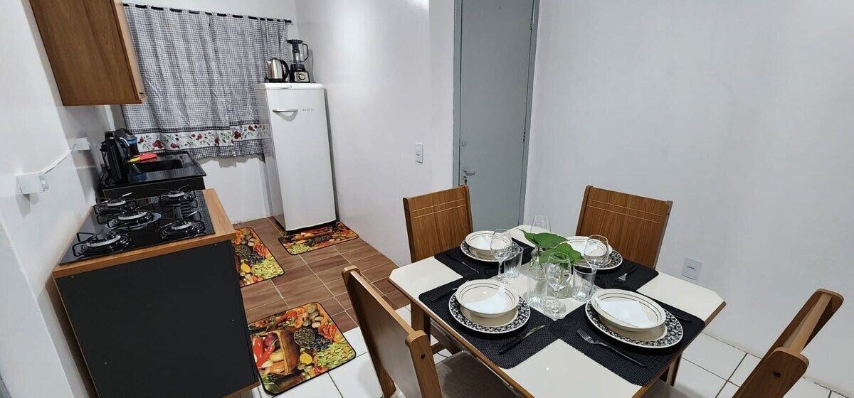 A compact kitchen with a gas stove, a small refrigerator, and a dining area with a table set for four.