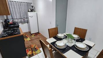 A compact kitchen with a gas stove, a small refrigerator, and a dining area with a table set for four.