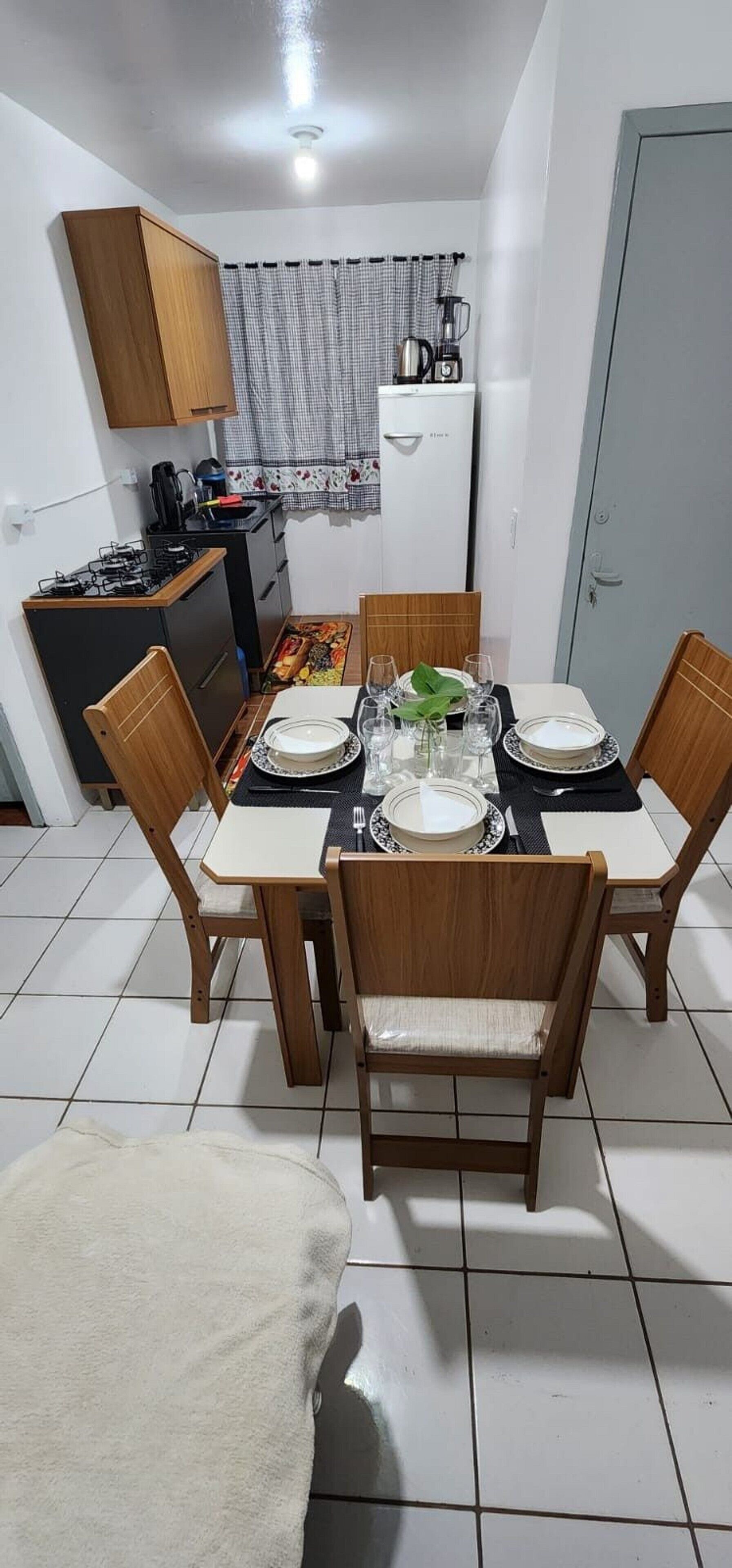 Een eethoek met een tafel gedekt voor vier personen, een keuken met een gasfornuis en een koelkast.