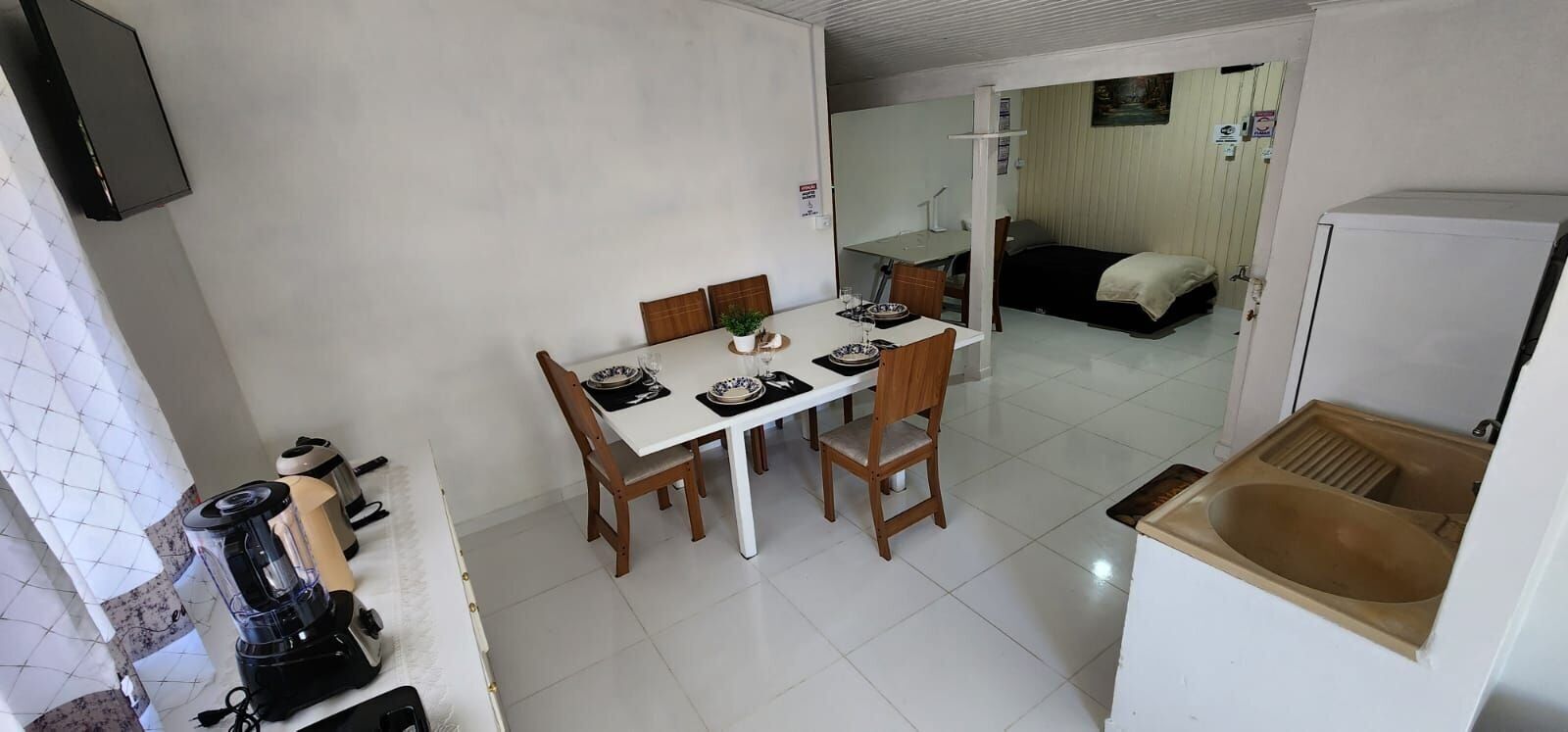 A compact hotel room with a dining table, chairs, a bed, a small kitchenette, and a bathroom with a shower.