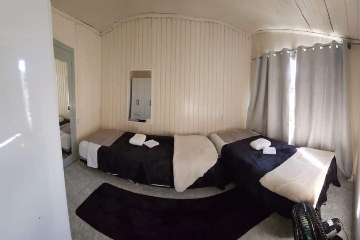 A compact room with two beds, a small table, and a mirror.