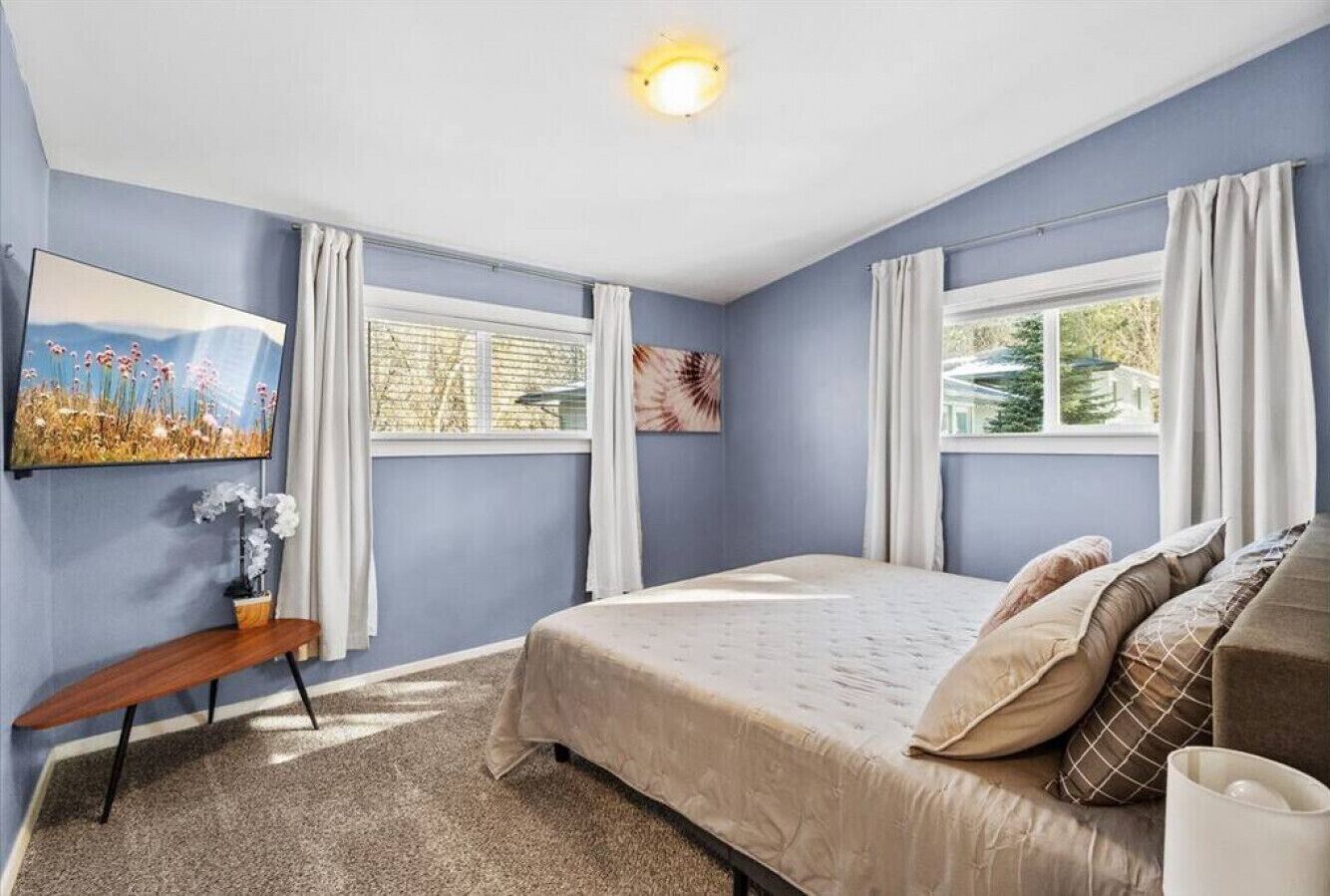 A bedroom with a bed, a desk, and a window with curtains.
