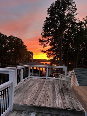 Een houten terras met een reling, uitkijkend op een wateroppervlak tijdens de zonsondergang.