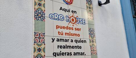 Une affiche en espagnol fait la promotion d’ARC HOUSE, en la présentant comme un lieu où l’on peut être soi-même et aimer la personne que l’on désire vraiment.