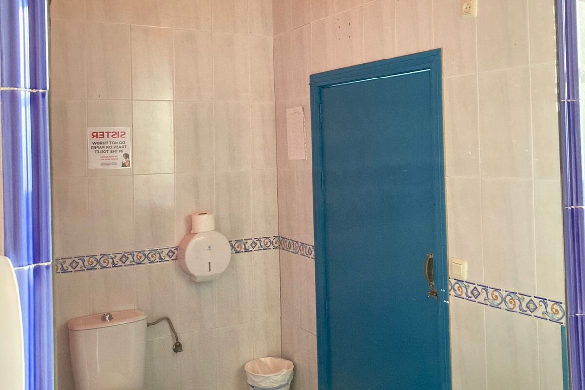 Un baño con puerta azul, inodoro, lavamanos y ducha.