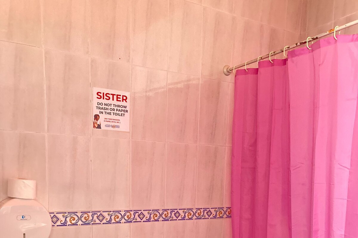Un baño con inodoro, cortina de ducha rosa y un cartel que indica no tirar basura ni papel en el inodoro.
