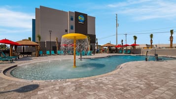 A swimming pool area with a water feature, lounge chairs, and umbrellas.