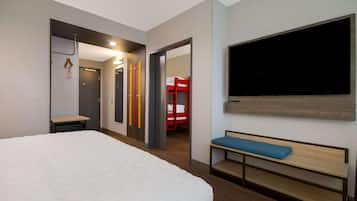 A hotel room with a large bed, a bench, a TV, and a red bunk bed in the adjacent room.