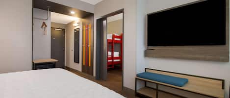 Ein Hotelzimmer mit einem großen Bett, einer Bank, einem Fernseher und einem roten Etagenbett im angrenzenden Raum.