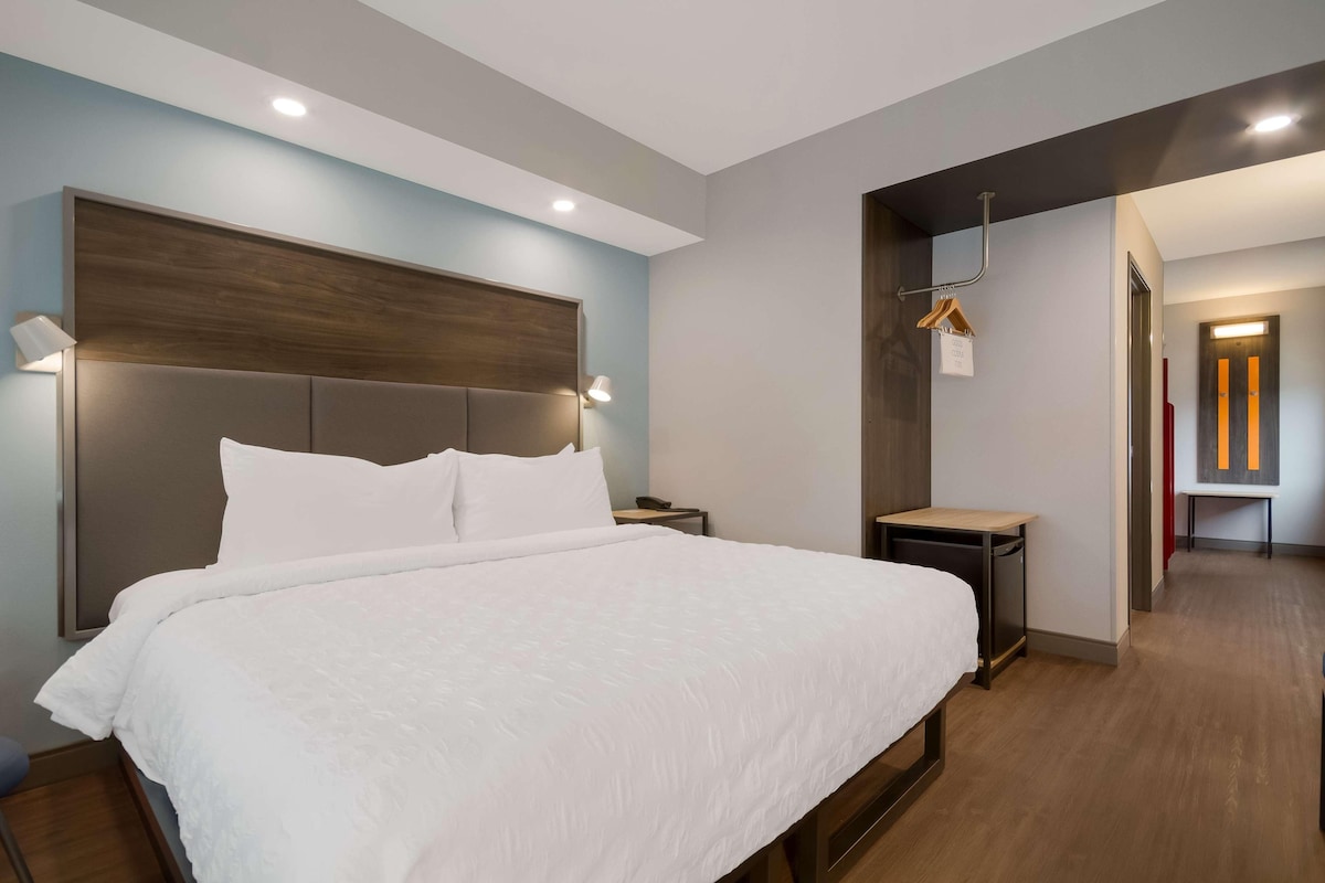 A modern hotel room with a large bed, bedside tables, and a wooden headboard.