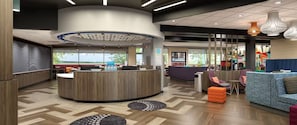 A modern reception area with a central desk, seating area with sofas, and a view of the outdoors. - Tru By Hilton Destin (Destin)