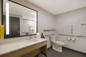 Une salle de bain moderne équipée d’un lavabo, d’un miroir, de toilettes et de barres d’appui.