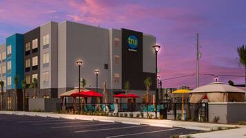 Un hotel modern amb un cartell ben visible de 'tru by Hilton', ombrelles exteriors i un aparcament.