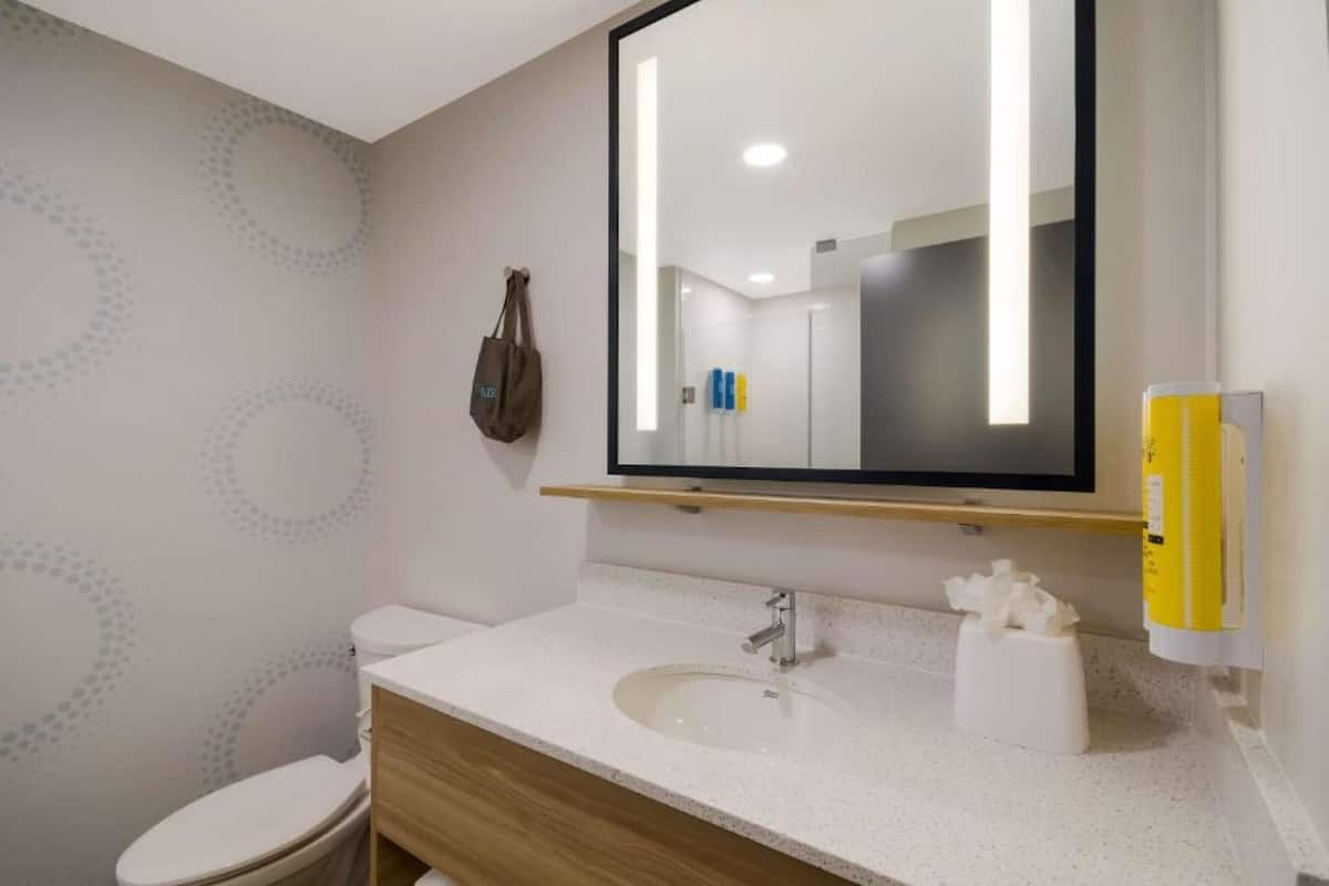 Un bagno moderno con un lavandino bianco, un mobile contenitore in legno e uno specchio grande.