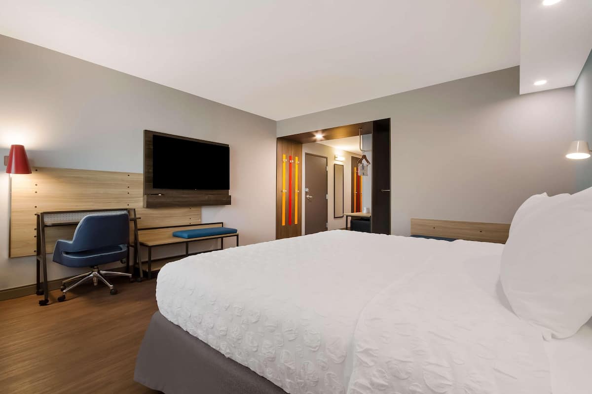 Una camera d'albergo con un letto grande, una scrivania con una sedia, una televisione e uno specchio.