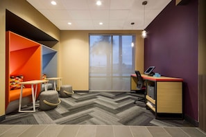 A modern office space with a herringbone-patterned carpet, a desk with a computer, and a colorful seating area with ottomans. - Tru By Hilton Destin (Destin)