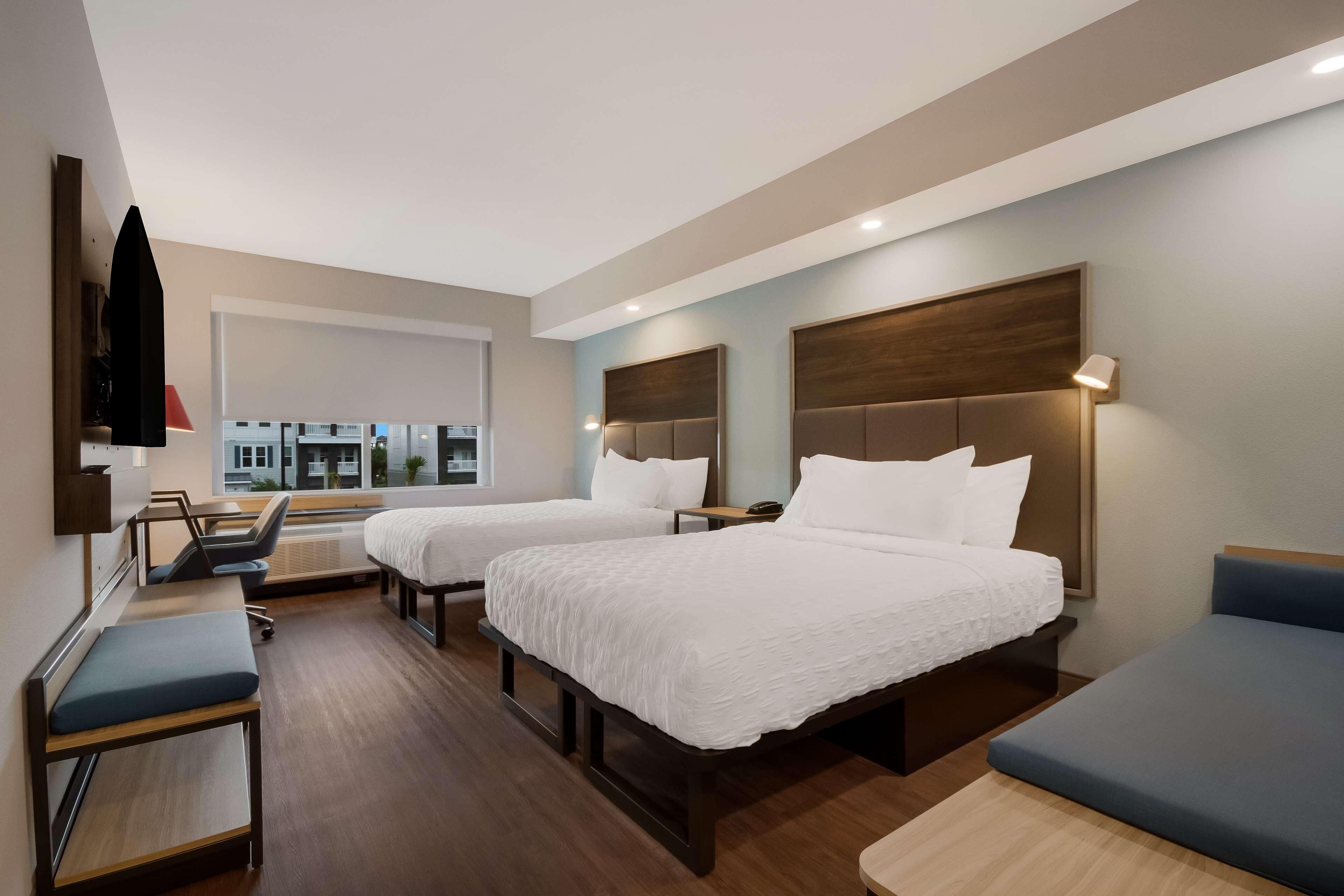 A hotel room with two beds, a desk, a chair, and a TV on the wall.