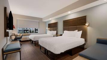 A hotel room with two beds, a desk, a chair, and a TV on the wall.