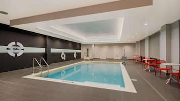 A swimming pool with a lifeguard station, red chairs, and a modern ceiling design.