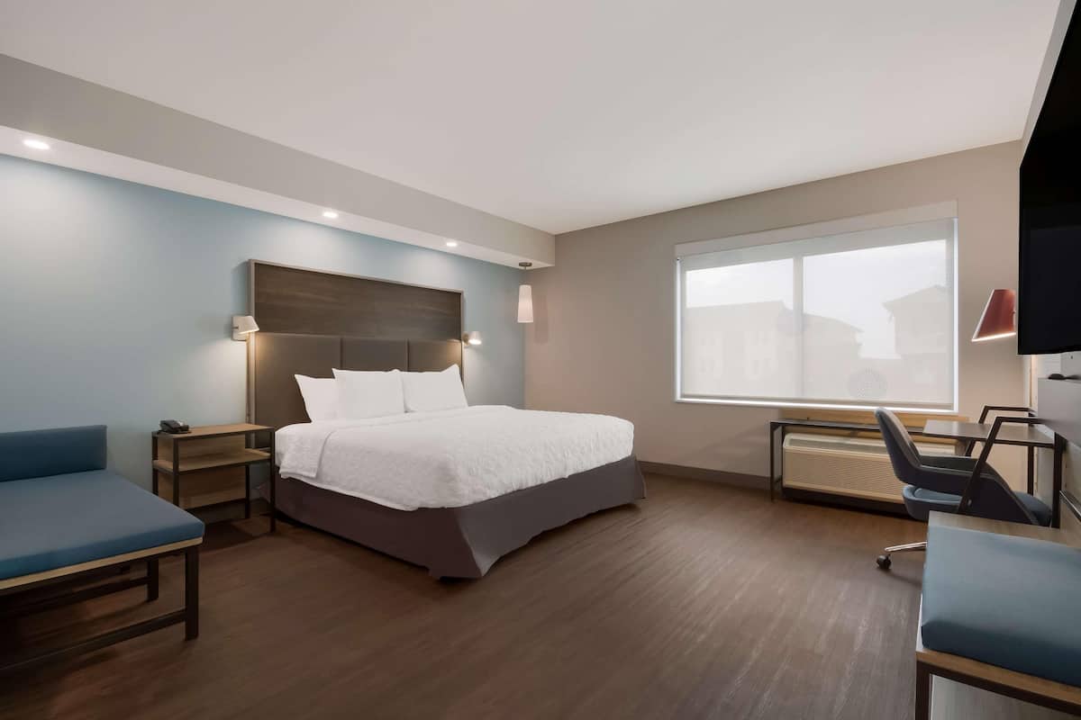 Una camera d'hotel moderna con un letto grande, una scrivania, una sedia e una televisione.