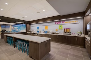 A modern breakfast area with a central island, bar stools, and a variety of breakfast items displayed on the counter. - Tru By Hilton Destin (Destin)