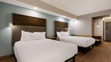 A hotel room with two beds, wooden headboards, bedside tables, and a small desk with a chair.