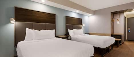 A hotel room with two beds, wooden headboards, bedside tables, and a small desk with a chair.