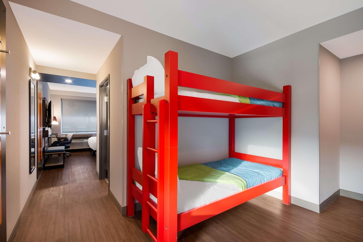 Habitación con literas, suelo de madera, escritorio con silla y espejo.