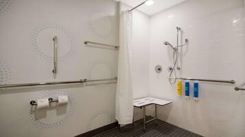 Bagno con WC, doccia dotata di maniglione, un piccolo tavolo e distributori di disinfettante per le mani.