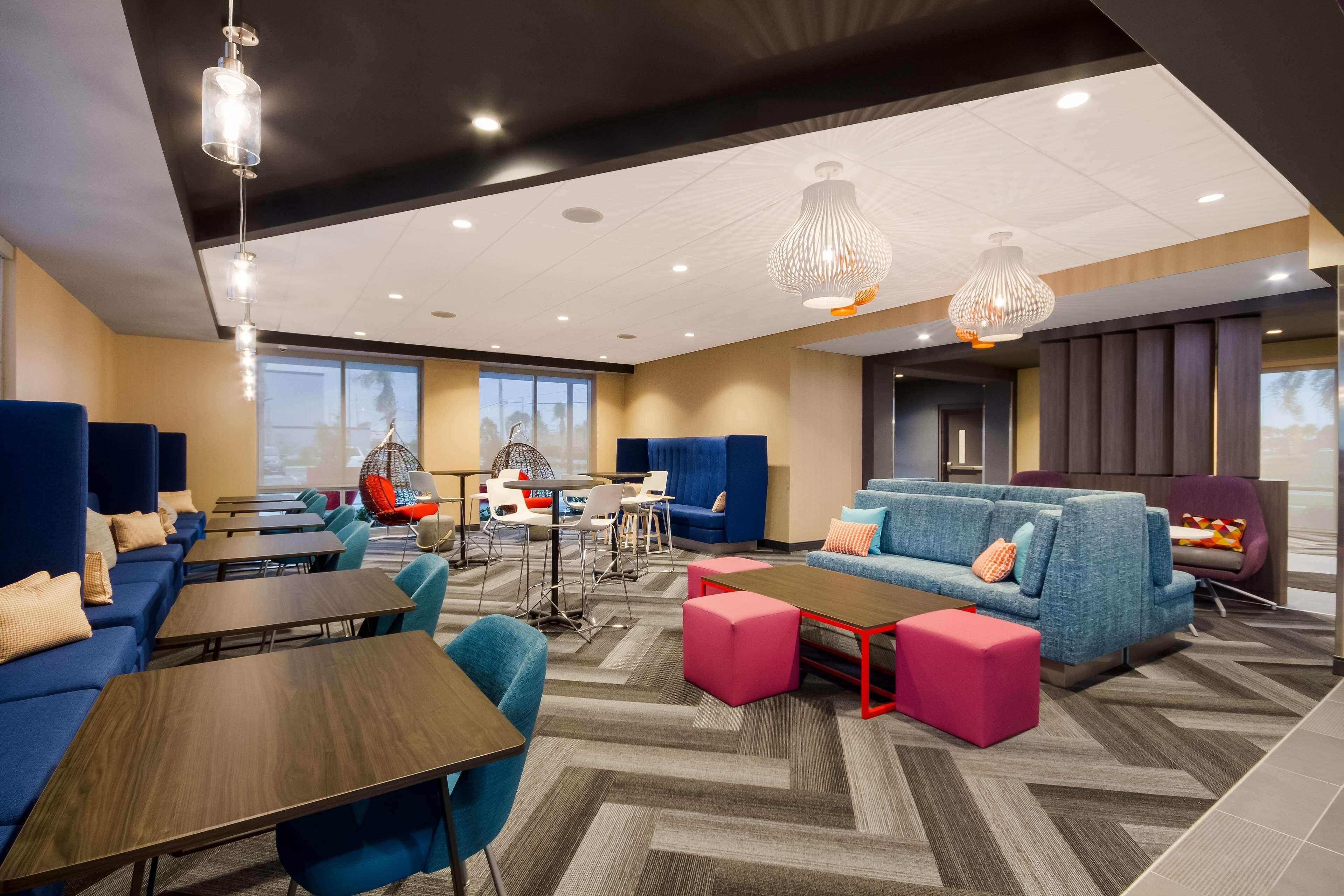 A modern hotel lobby with blue sofas, wooden tables, and a mix of seating options including chairs and ottomans.