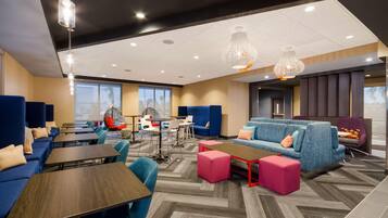 A modern hotel lobby with blue sofas, wooden tables, and a mix of seating options including chairs and ottomans.