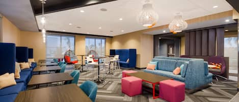 A modern hotel lobby with blue sofas, wooden tables, and a mix of seating options including chairs and ottomans.
